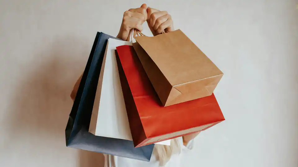 Pessoa segurando várias sacolas de compras coloridas em frente a uma parede branca