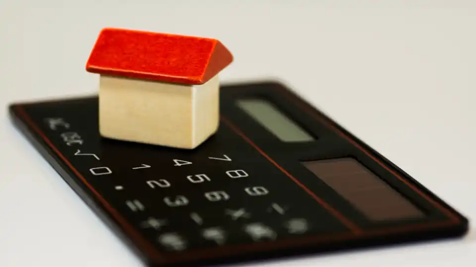 Casinha de madeira de telhado vermelho sobre uma calculadora preta