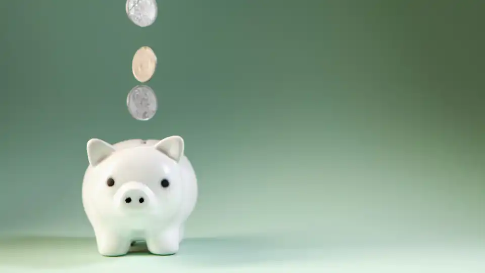 Moedas caindo dentro de um cofrinho branco em formato de porco