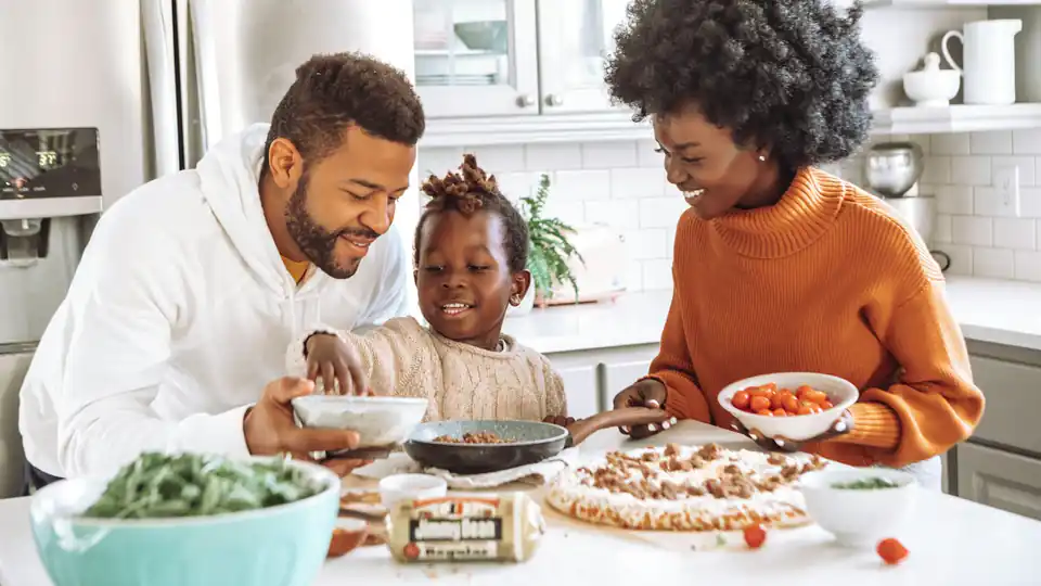 Pai, mãe e filha preparando comida juntos na mesa da cozinha