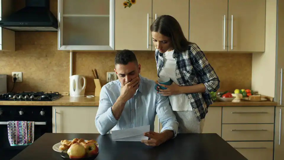 Casal na cozinha lendo uma conta com expressão preocupada