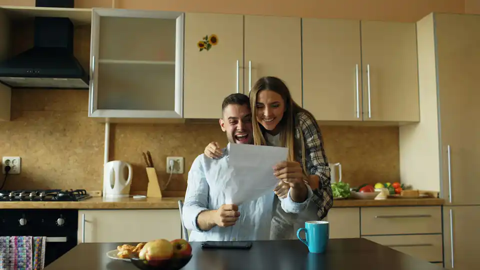 Casal na cozinha olhando um documento com expressão animada