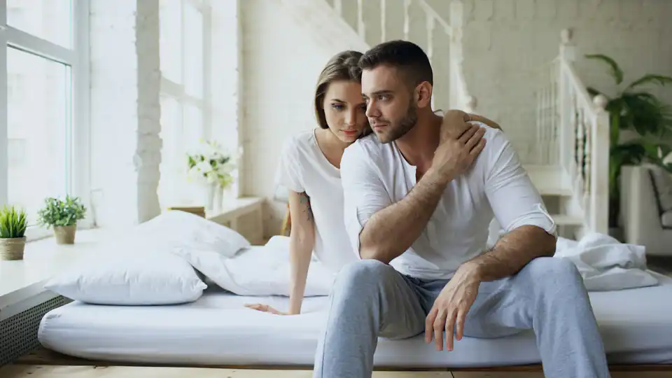 Casal sentado na cama de um quarto claro conversando